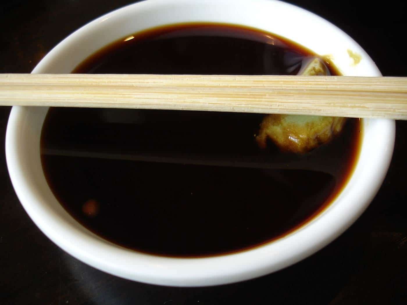 A small bowl of soy sauce with wasabi and chopsticks
